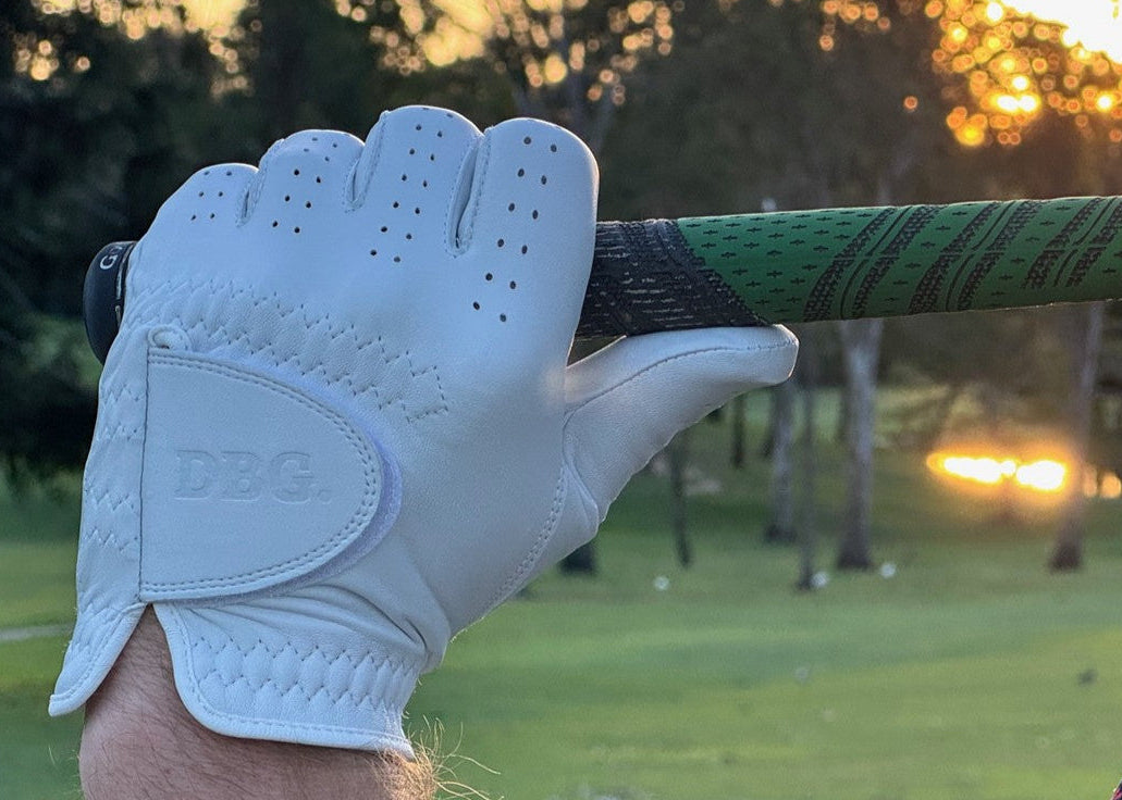 Golf club with a white glove held by a person on a golf course at sunset.