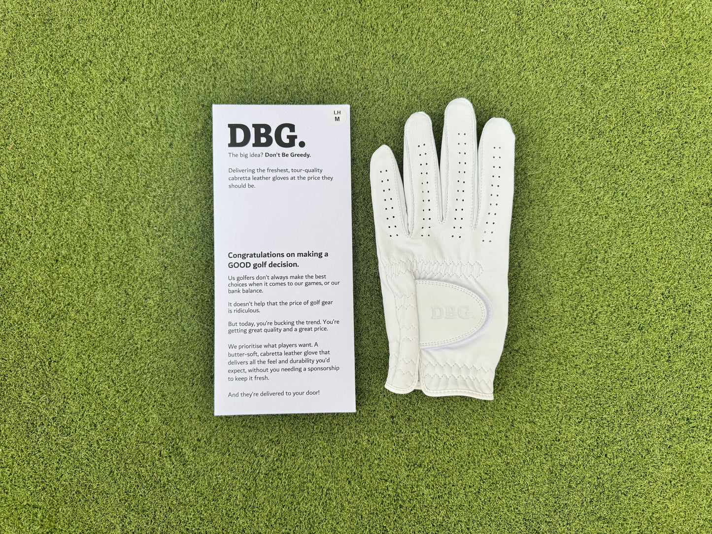 White golf glove and DBG branded packaging on a green surface
