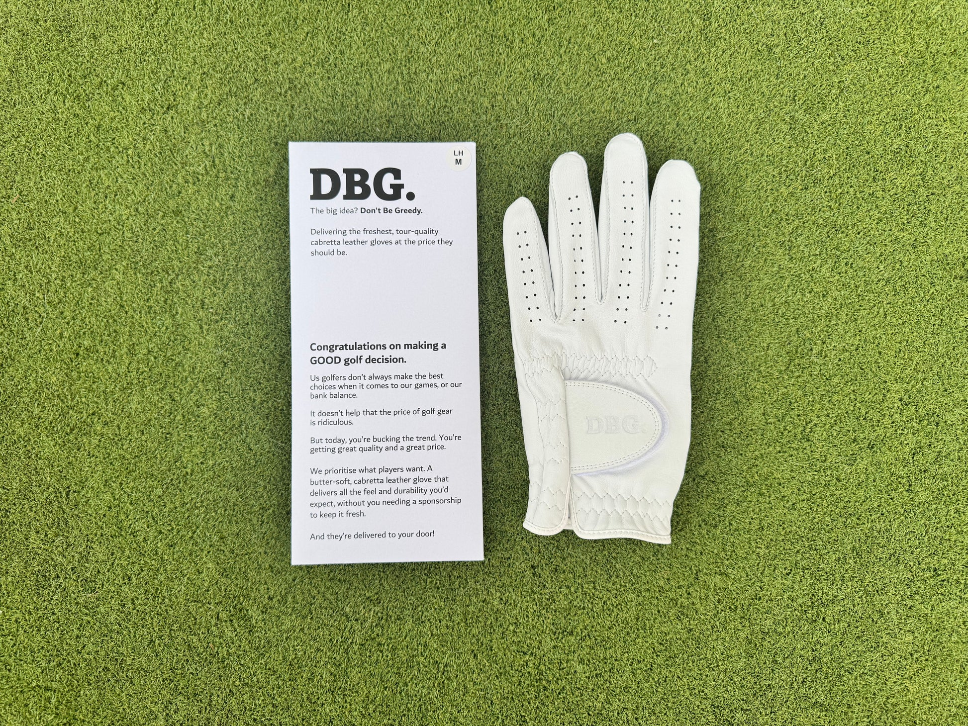 White golf glove and DBG branded packaging on a green surface