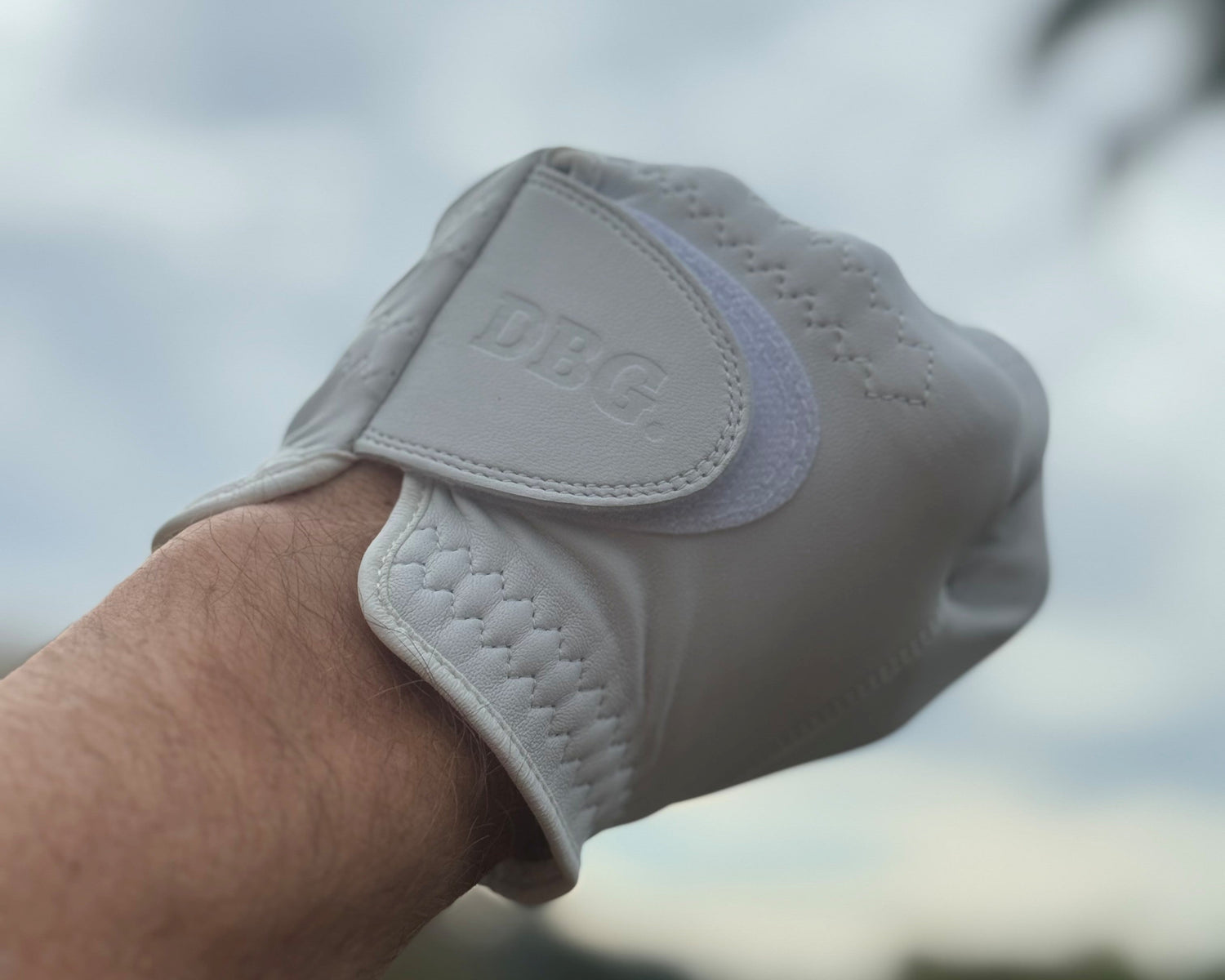 White golf glove with 'DBG' branding on a blurred natural background